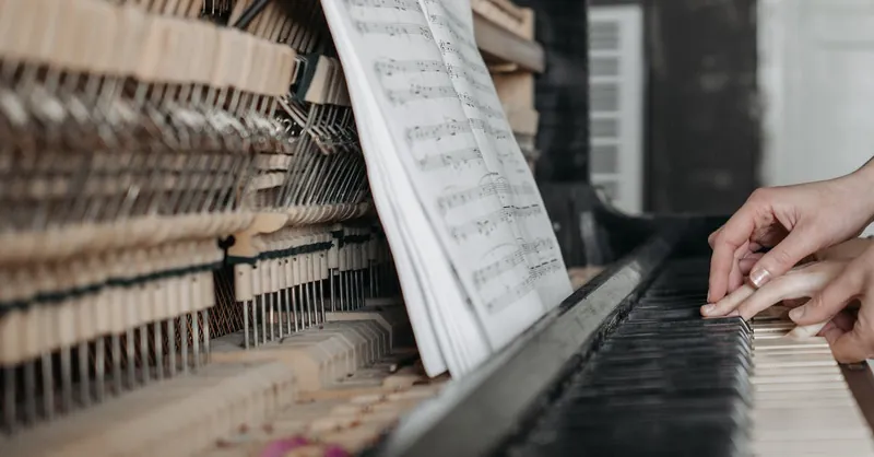 Close-up of hands playing piano keys with open sheet music, emphasizing learning and teaching.