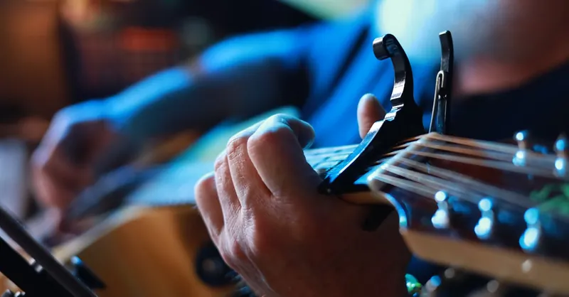 Detailed view of hands playing guitar with capo, capturing musician