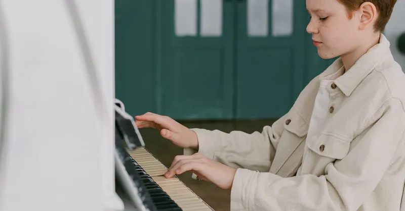 Boy with freckles playing piano in an indoor setting, focused and practicing diligently.
