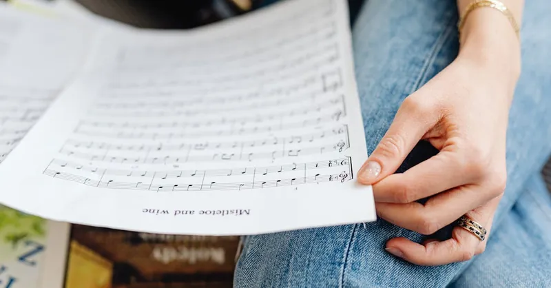 An adult hand holding musical sheets, wearing a ring and bracelet, focusing on music practice.