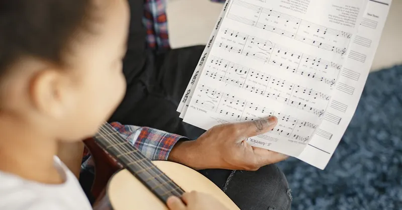 A young girl learning guitar with a teacher, focusing on a music sheet.