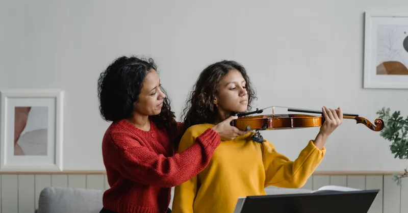 A woman teaches a young girl to play violin during a lesson at home, promoting music education.