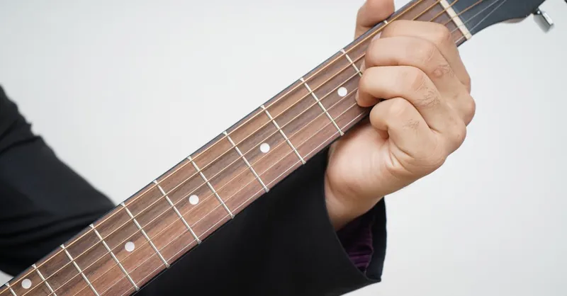 A detailed close-up of a hand playing a chord on an acoustic guitar neck.
