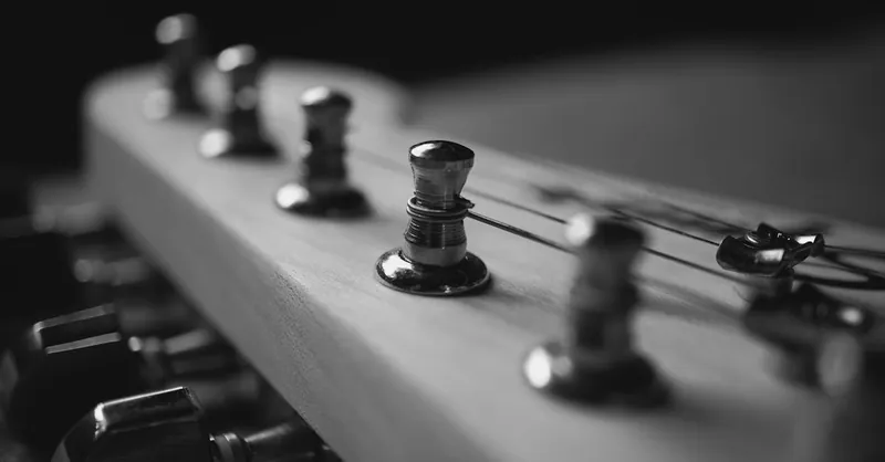 Black and white close-up of guitar headstock with tuning pegs.