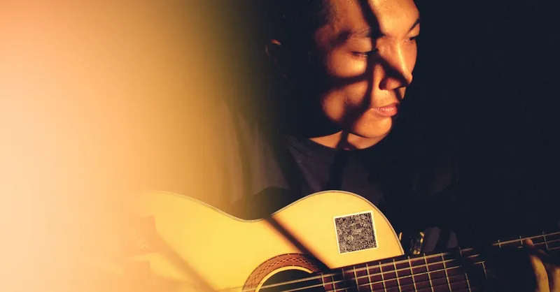 Close-up of a musician playing an acoustic guitar in warm, moody lighting, capturing a moment of creativity.