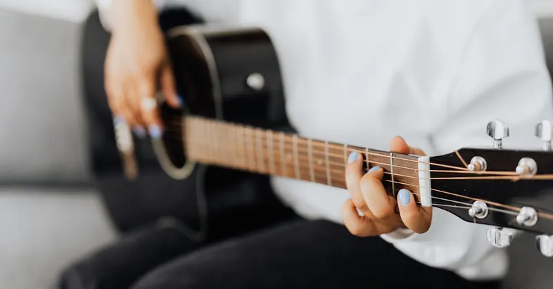 Person playing an acoustic guitar. Focus on fretboard and hand positioning.