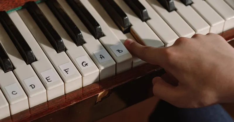 A person playing a labeled piano keyboard with finger pressing notes for learning music.