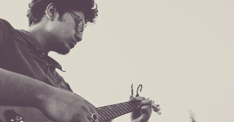 A black and white side view portrait of a male guitarist playing solo outdoors.