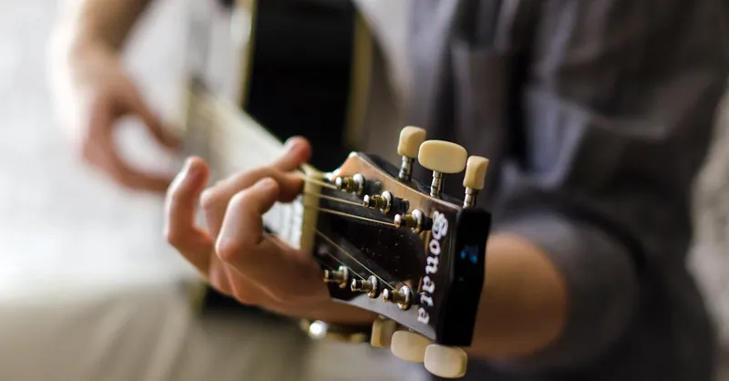 Close-up view of a guitar headstock being played, highlighting the tuning keys and strings.