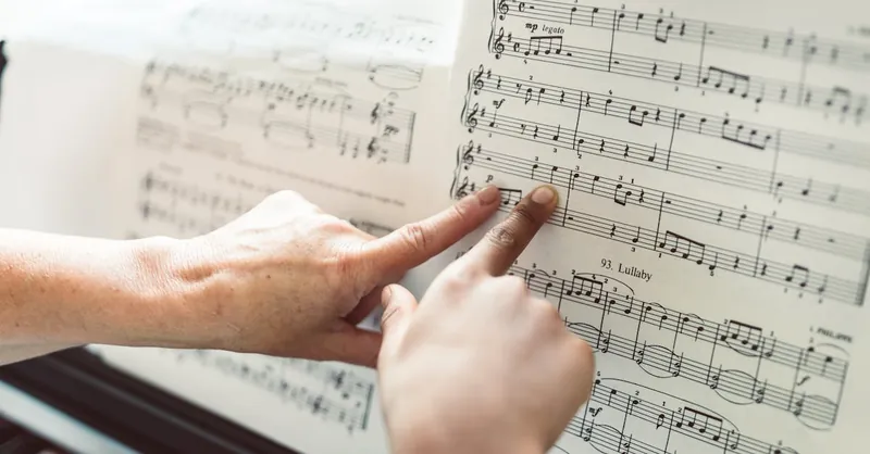 Close-up of hands pointing to notes on a music sheet during a piano lesson, highlighting music education.