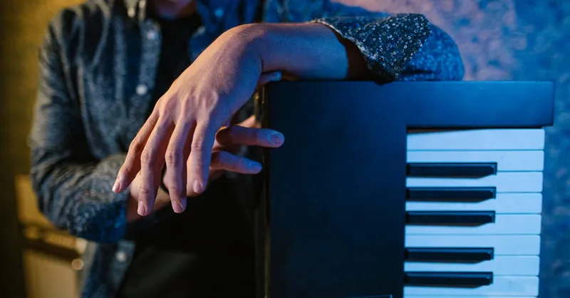 A musician leaning on a keyboard piano in a stylish, artistic setting.