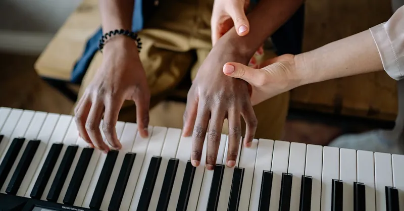 A music teacher guides a student on piano keys, emphasizing hands-on learning.