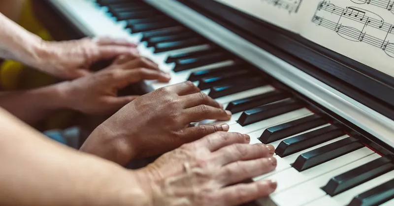 Close-up of hands playing a piano with visible sheet music, showing a teaching tutorial.