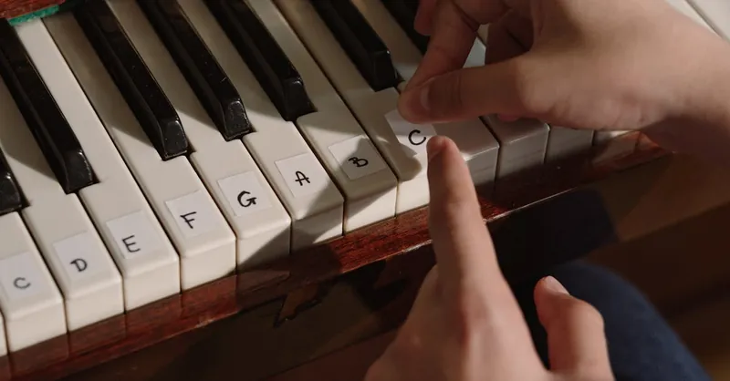Hands labeling piano keys for beginners. Close-up of a finger pointing at a labeled key.