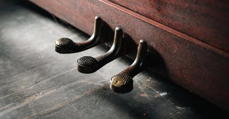 Artistic close-up of antique piano pedals against wooden flooring.