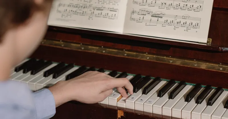 A person playing a piano with a focus on hands and sheet music, highlighting musical practice.