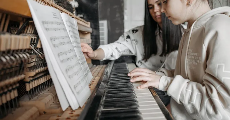 A child learning to play piano with guidance from an adult in a cozy setting, focusing on music sheets.