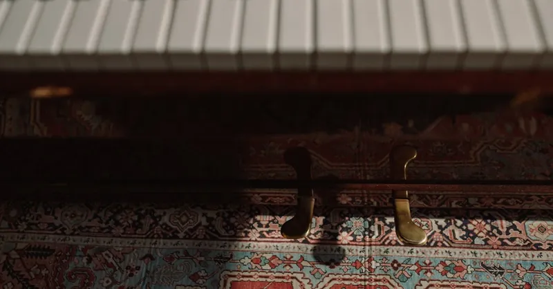 Artistic close-up of piano keys and pedals over vibrant patterned carpet in low light.